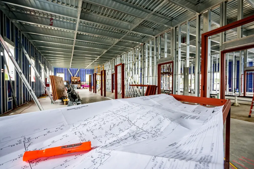 Steel-stud interior framing with construction drawings laid out on a table