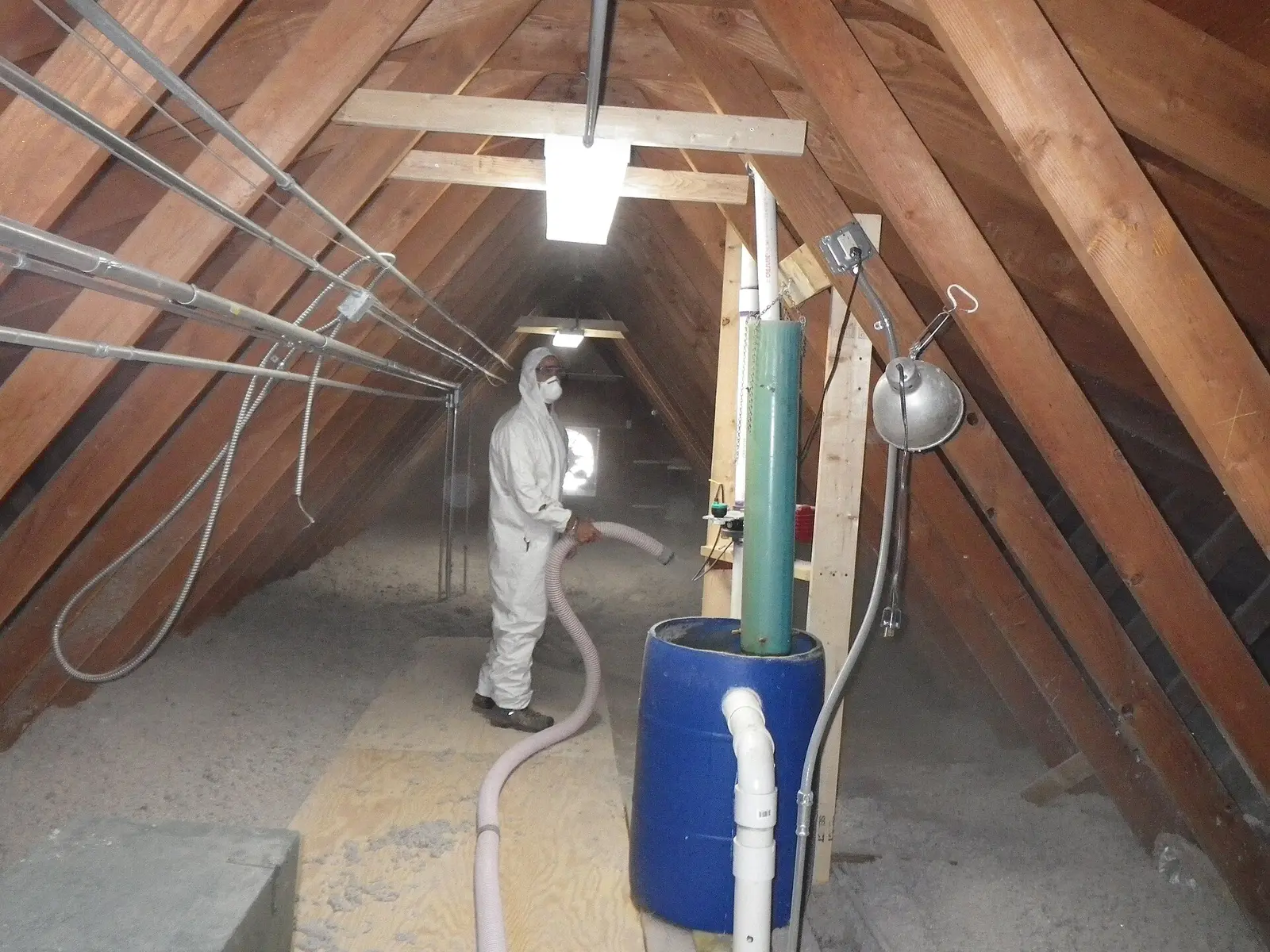 Installer in coveralls blowing insulation into an attic through a hose
