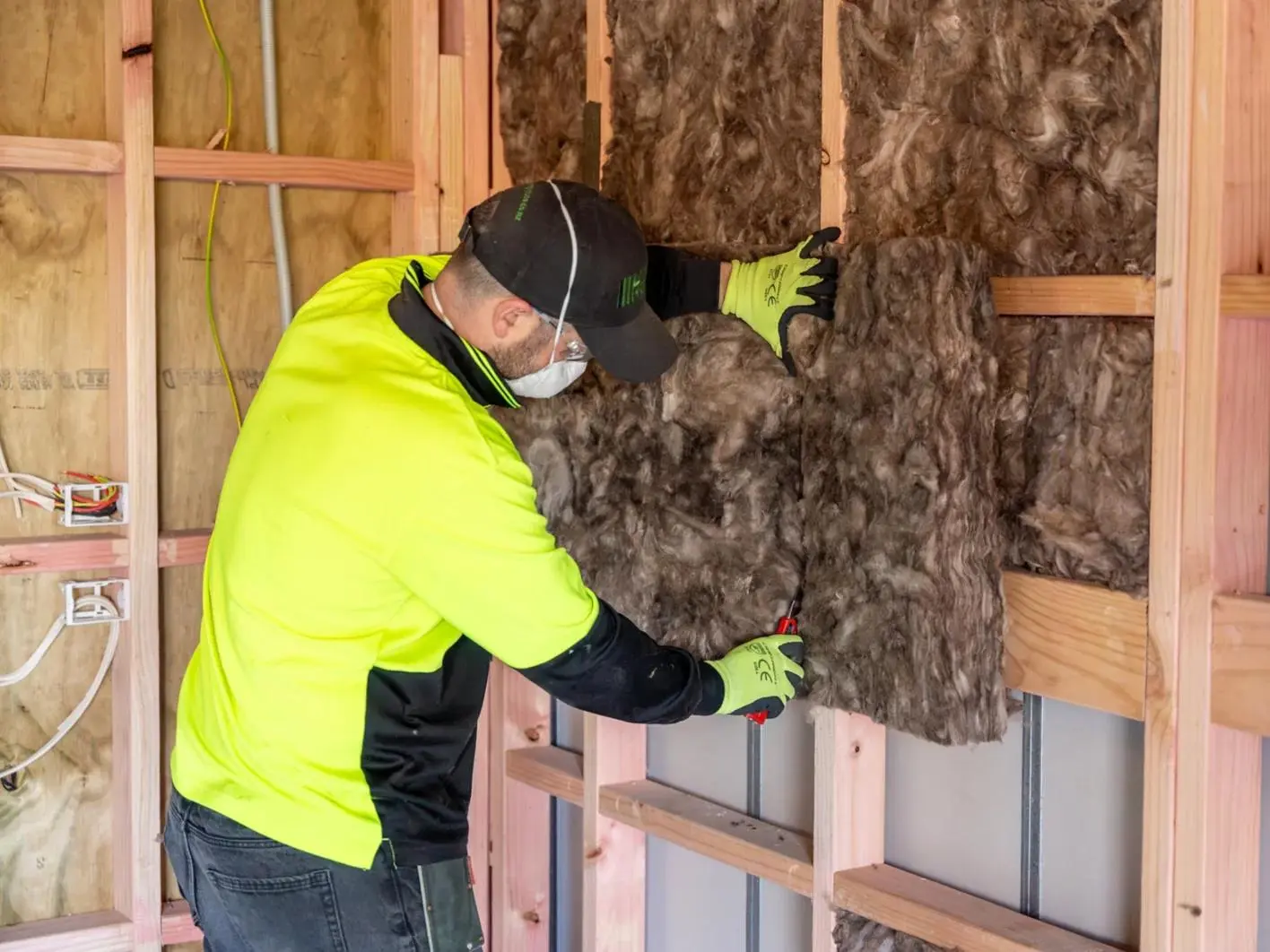 Installer fitting glass-wool batts between wood studs in an open wall