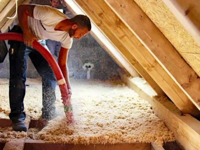Loose-fill fiberglass being blown through a hose onto an attic floor