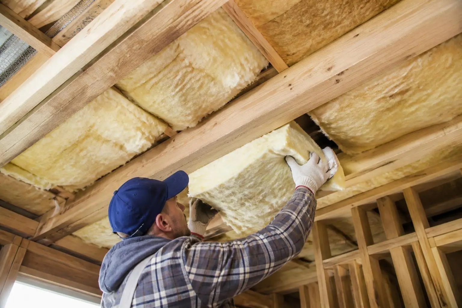 Installer fitting fiberglass batts between ceiling joists