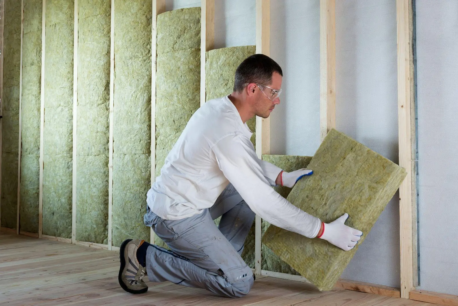 Installer placing mineral-wool batts into a framed interior wall